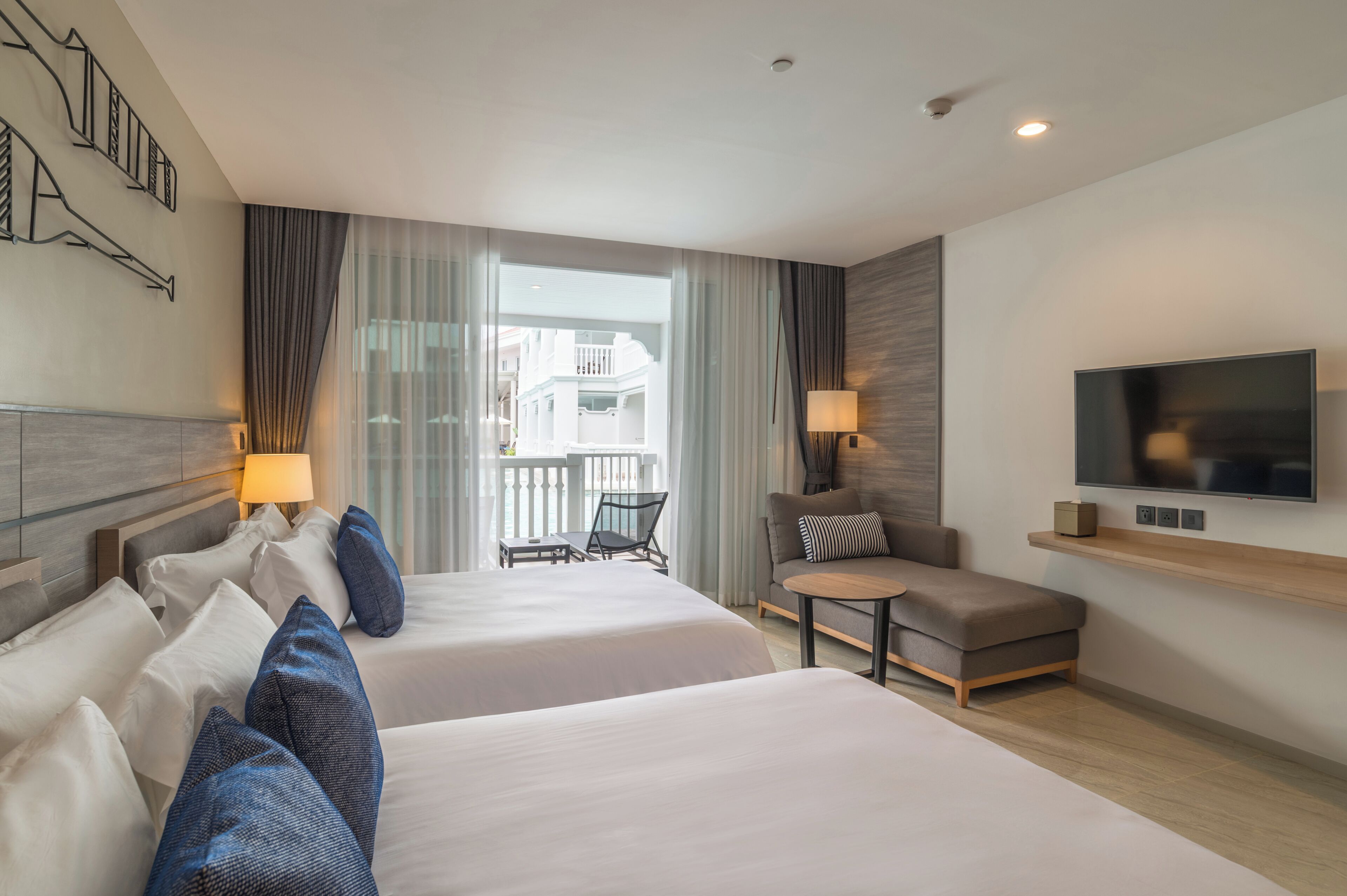 Une chambre d’hôtel avec deux lits, un canapé, une télévision et un balcon donnant sur des immeubles.
