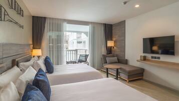 Une chambre d’hôtel avec deux lits, un canapé, une télévision et un balcon donnant sur des immeubles.