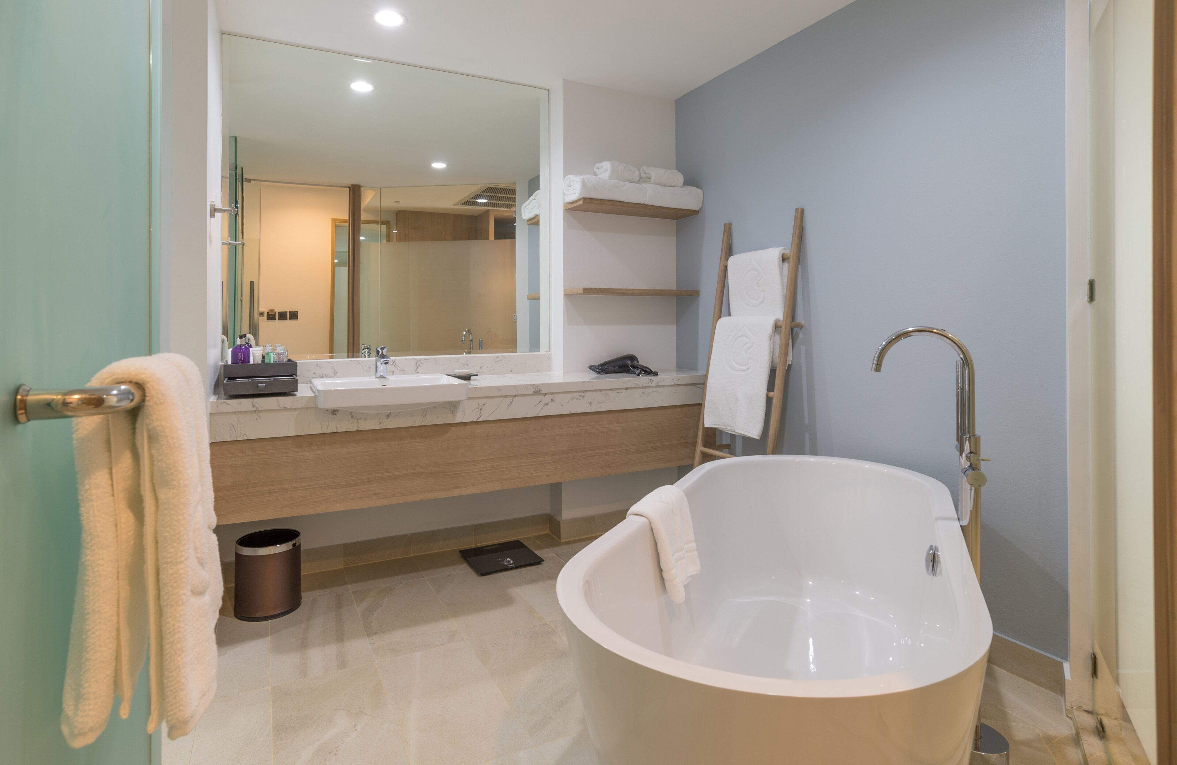 A modern bathroom with a freestanding bathtub, a large mirror, and a vanity with a sink and towel rack.