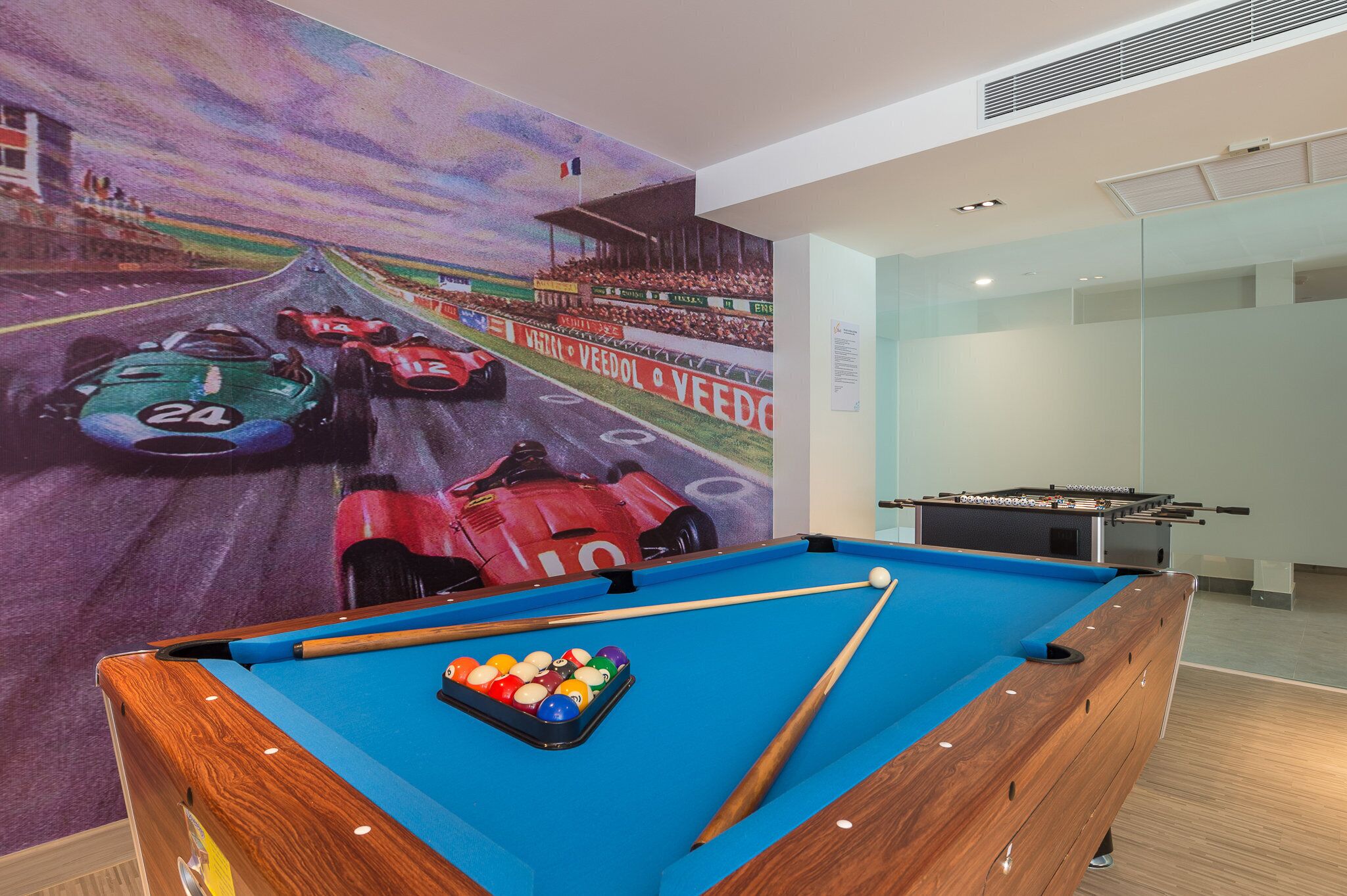 A pool table with a colorful ball rack in the foreground and a racing car mural on the wall behind it.