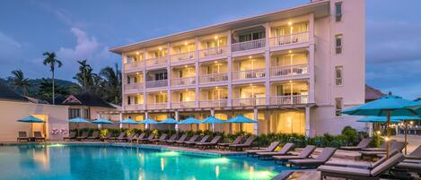A hotel with a swimming pool, multiple balconies, and lounge chairs.