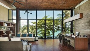 Una habitación amplia con un gran ventanal que da a un paisaje tropical, techo de madera y un mostrador de recepción.