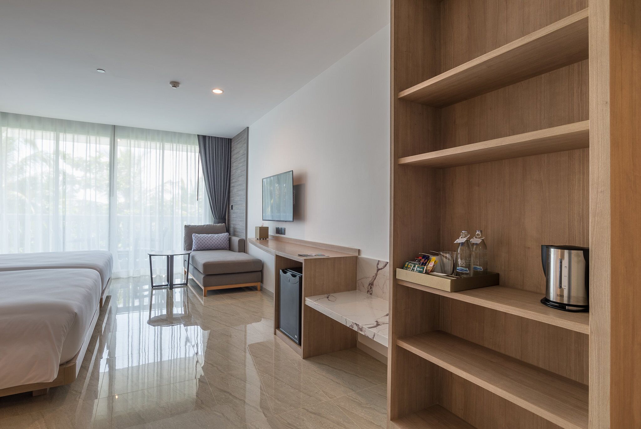 A modern hotel room with a large bed, a desk, a sofa, and a wooden shelving unit.
