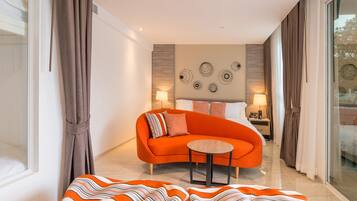 Una habitación de hotel moderna con un sofá naranja curvo, una mesa redonda pequeña y una cama con cabecera.