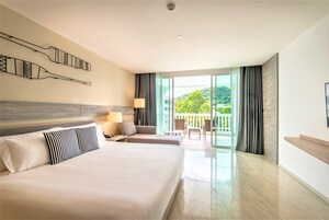 Habitación de hotel con una cama grande, un escritorio, una silla y un balcón con vistas a zonas verdes.