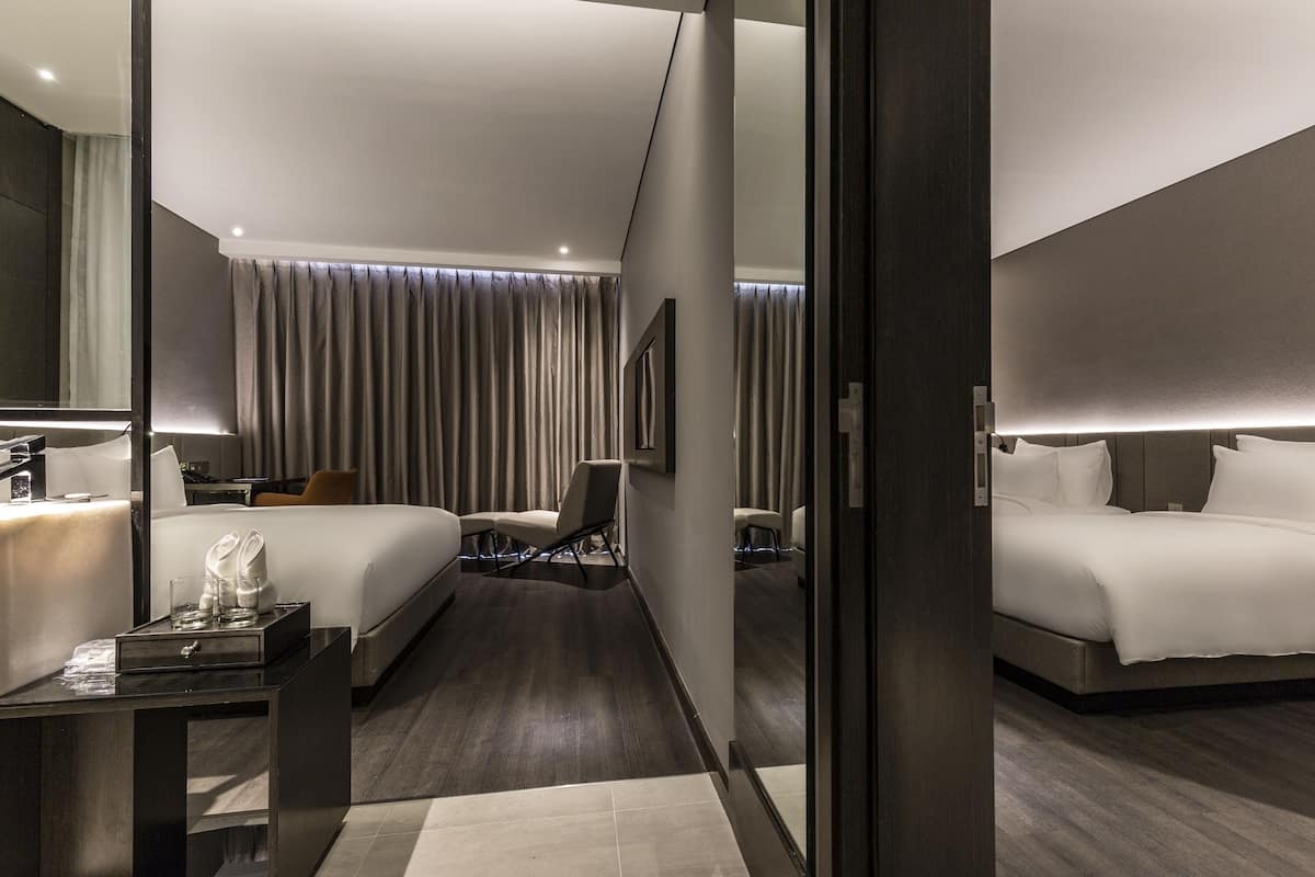 A modern hotel room with a large bed, a desk with a chair, a small table with a tray, and a mirror.