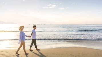 Två personer går längs en strand och håller varandra i handen.