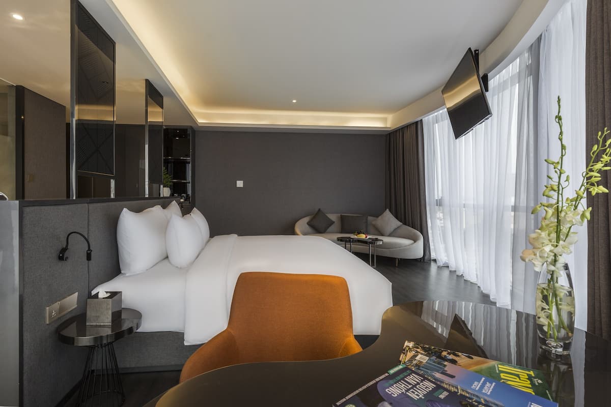 A modern hotel room with a large bed, a sofa, a small table, and a TV mounted on the wall.