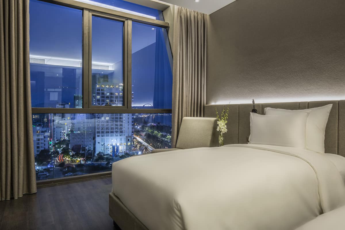 A hotel room with a large window, a bed, and a view of the city at night.
