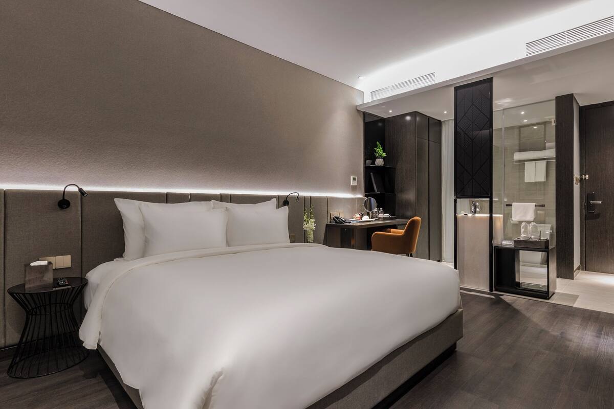 A modern hotel room with a large bed, bedside table, and a desk area.