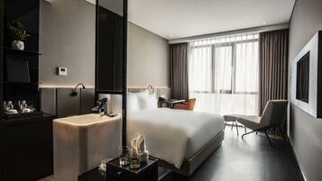 Una habitación de hotel moderna con una cama grande, un escritorio, una silla, un tocador con espejo y una planta en maceta.