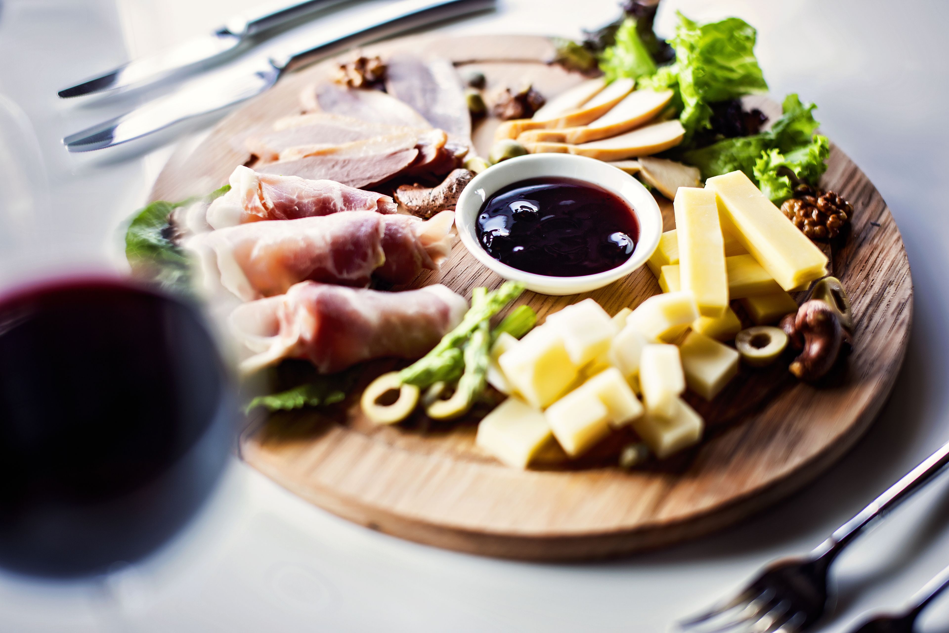 A wooden board with various cheeses, meats, and vegetables, accompanied by a small bowl of sauce.