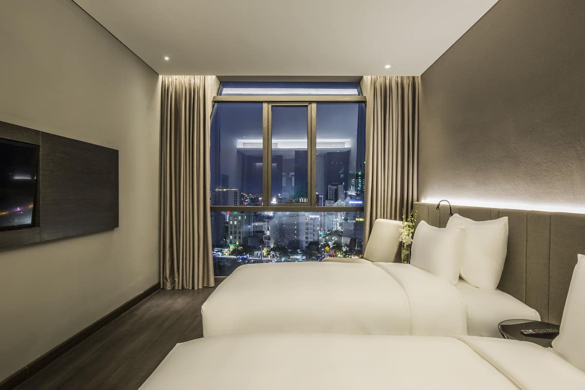 A modern hotel room with a large bed, a TV mounted on the wall, and a city view through the window.