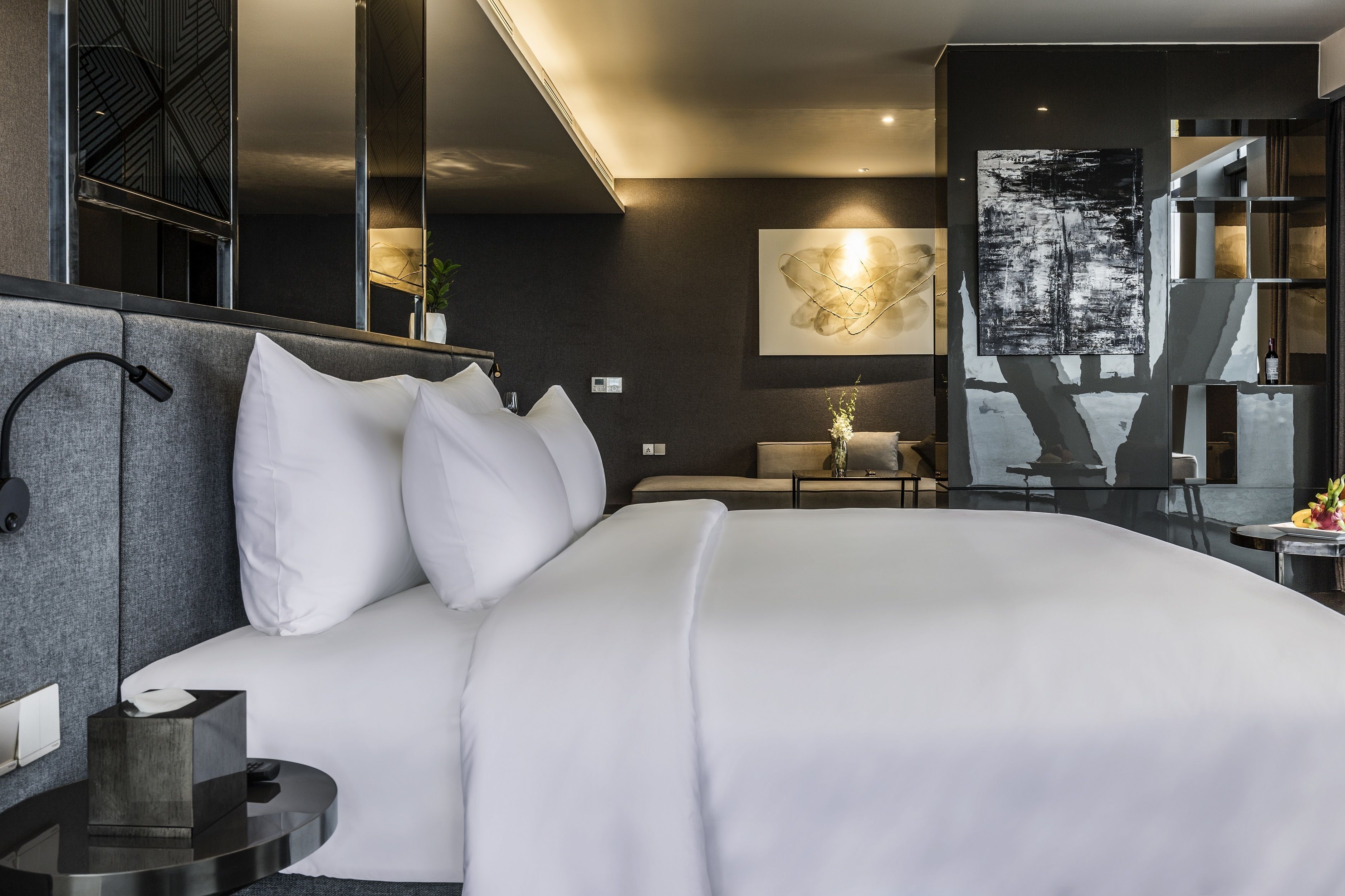 A modern hotel room with a large bed, a bedside table, a lamp, and a wall-mounted artwork.