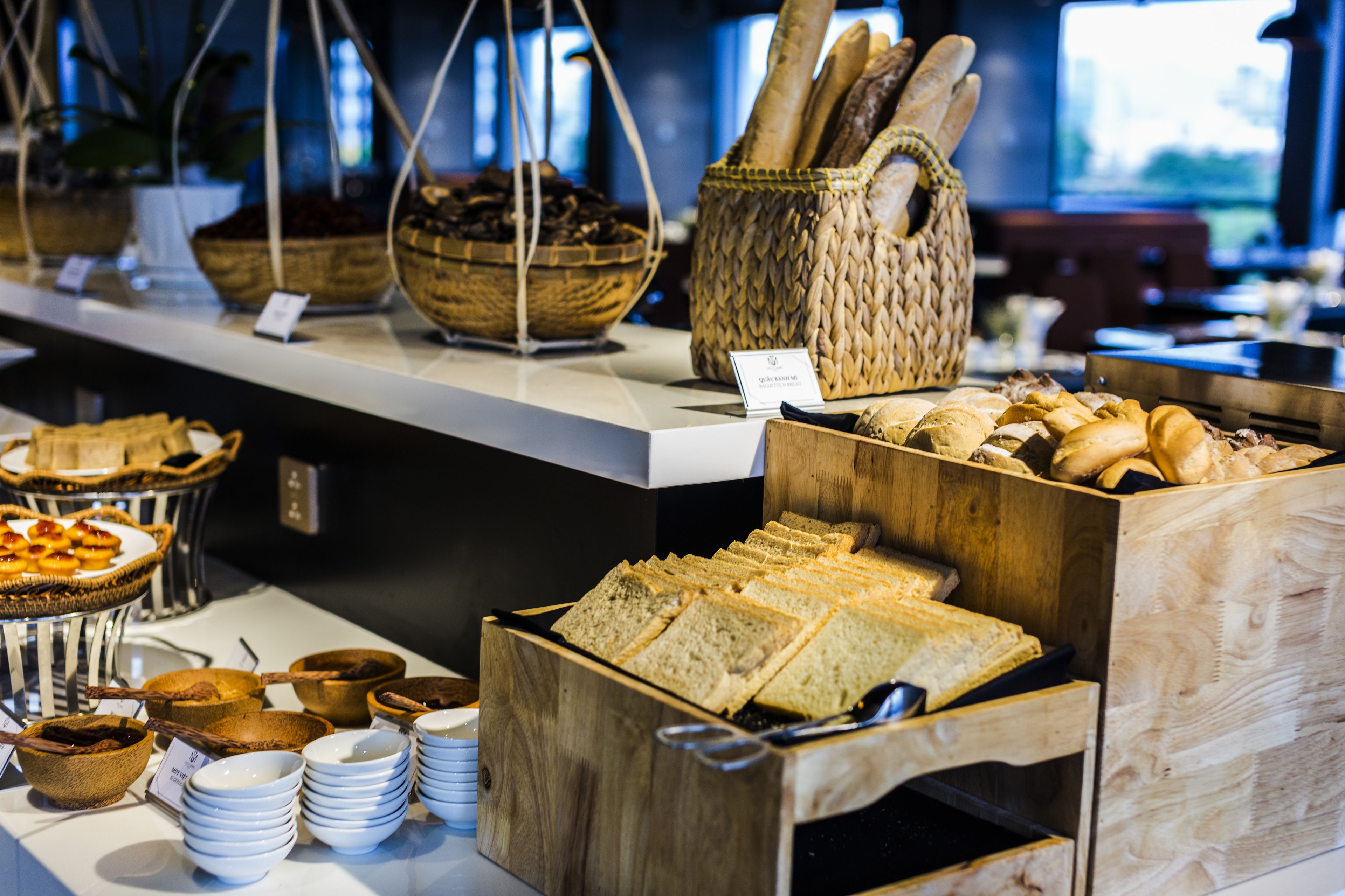 A buffet with various bread and pastries displayed in baskets and wooden boxes.