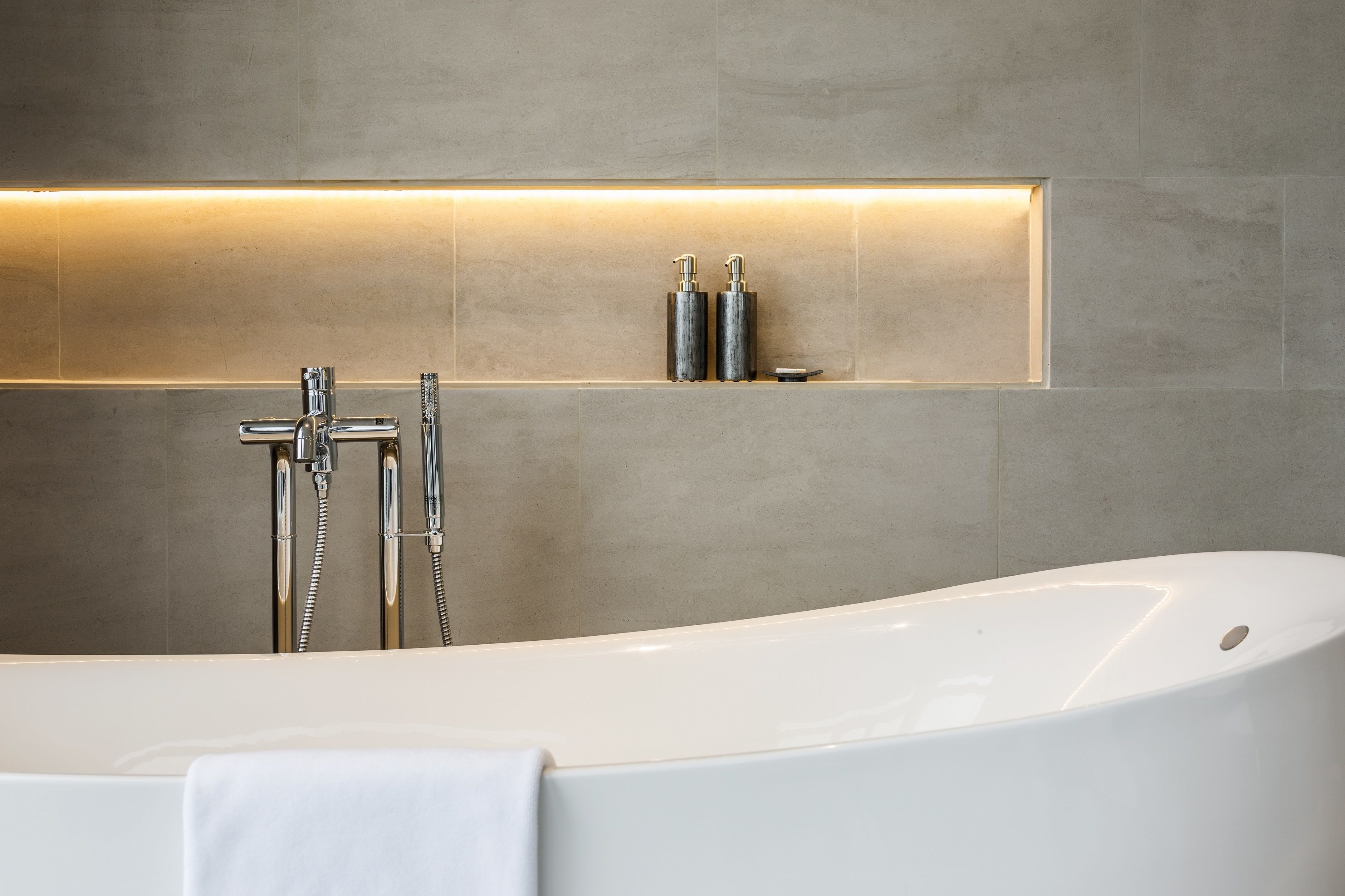 A modern bathroom with a freestanding bathtub, a wall-mounted showerhead, and two bottles of shampoo on a shelf.