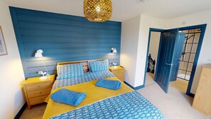 A bedroom with a bed, bedside tables, lamps, and a blue-patterned headboard. - Sandy Shores - a cottage that sleeps 4 guests in 2 bedrooms (Filey)