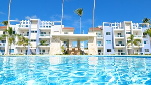 Een hotel met een zwembad, palmbomen en een helderblauwe lucht.