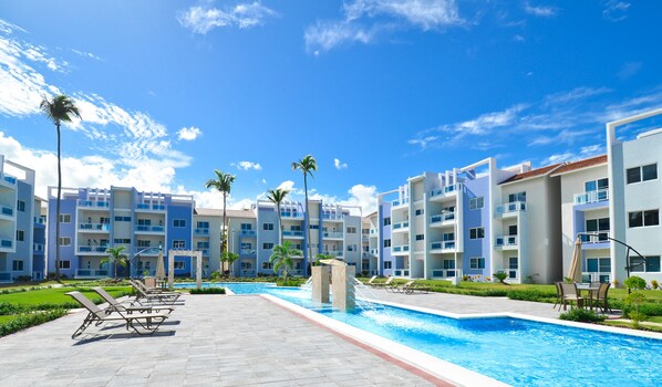 A resort with a swimming pool, palm trees, and modern buildings. - 2 Bedroom, 2 Bath Ground Level Condo (Punta Cana)