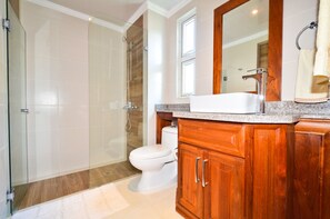 A bathroom with a glass shower enclosure, a white toilet, wooden cabinets, and a large mirror above the sink. -  2 Bedroom, 2 Bath Ground Level Condo (Punta Cana)