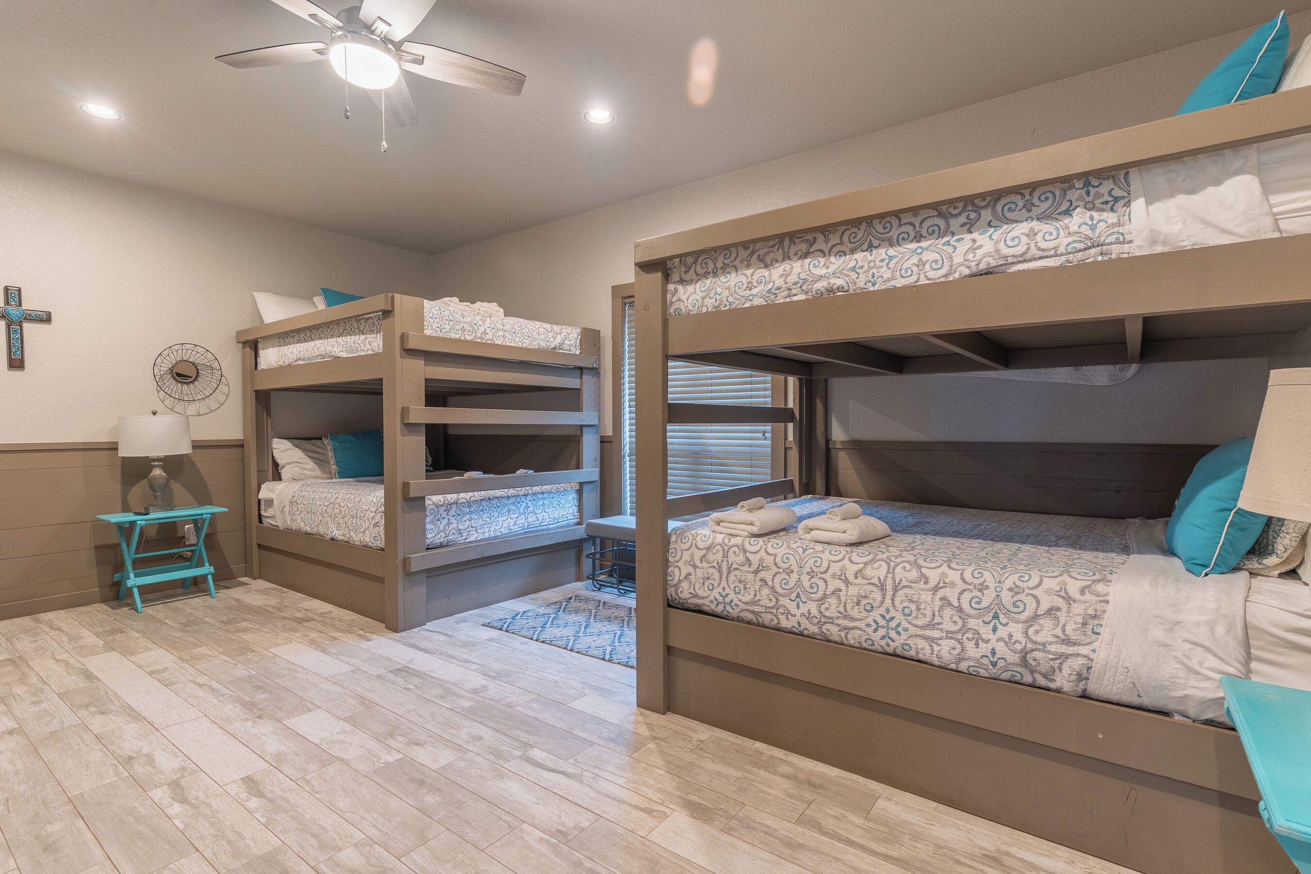 A room with two bunk beds, a small table with a lamp, and a ceiling fan.