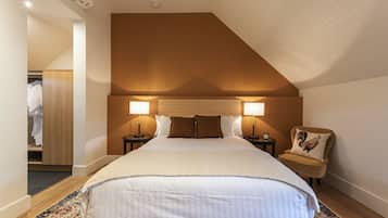 A bedroom with a large bed, two bedside lamps, a nightstand, a chair with a cushion, and a wooden wardrobe.