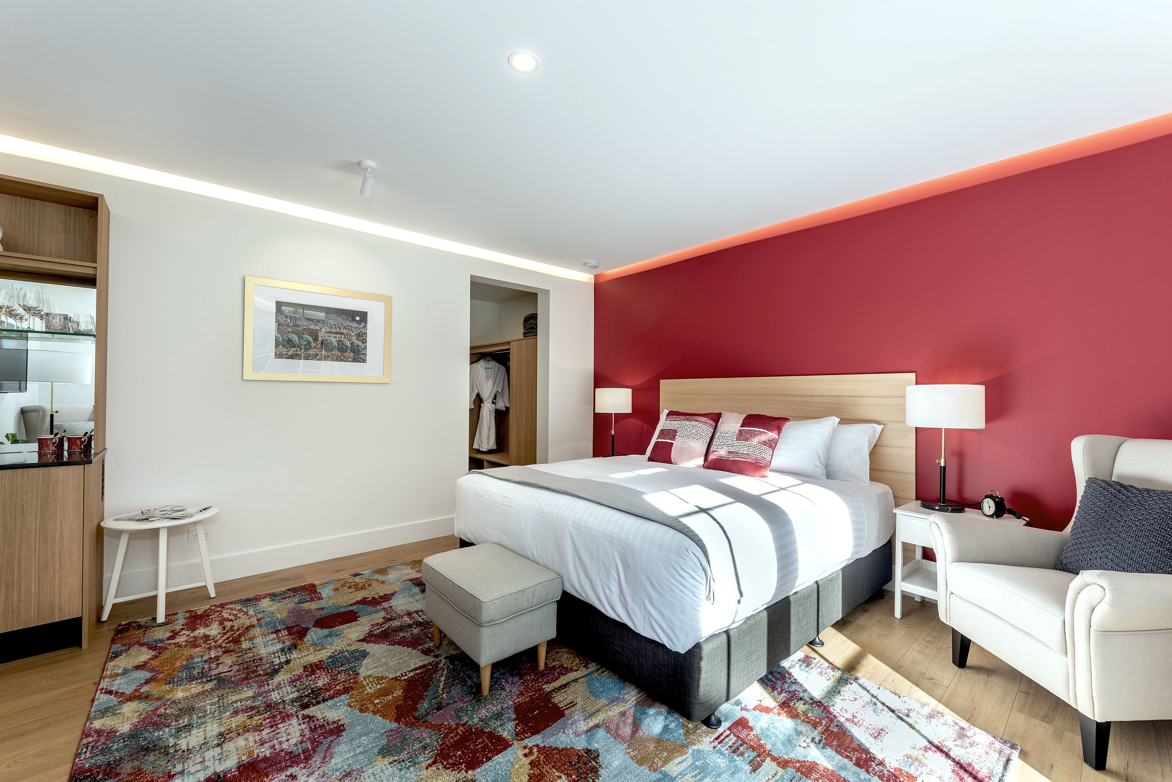 A modern bedroom with a large bed, a nightstand, a chair, a small table, and a wardrobe.