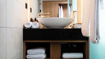 Un baño moderno con un lavamanos grande de color blanco, estantes de madera con toallas dobladas y un espejo que refleja un armario y toallas.