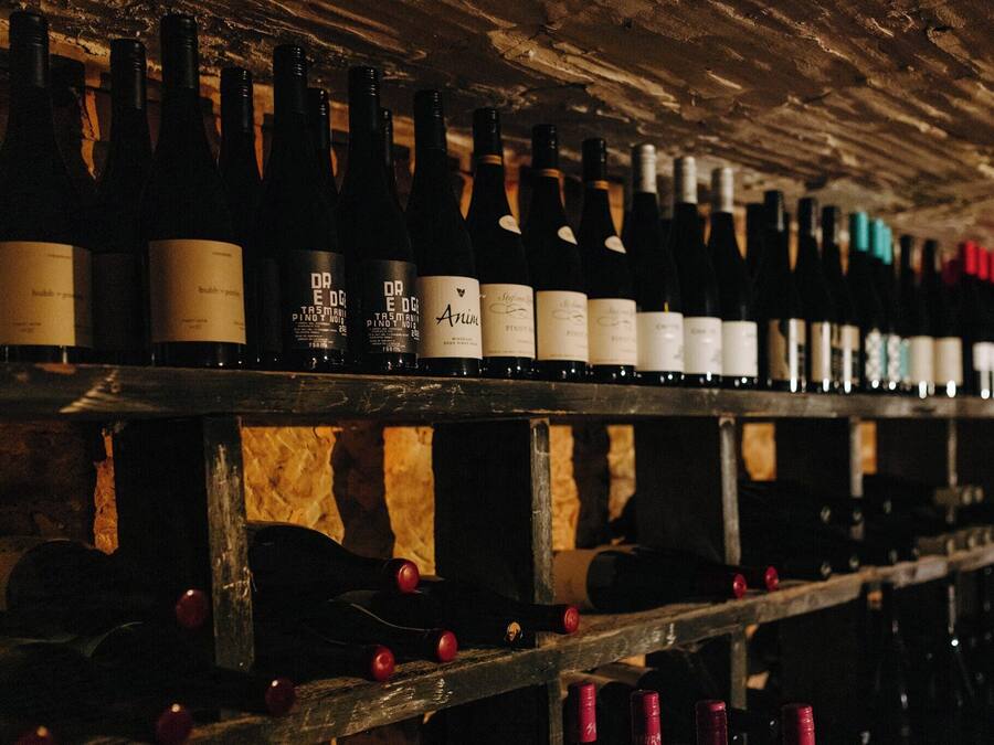 Botellas de vino alineadas en estantes de madera en una bodega tenuemente iluminada.