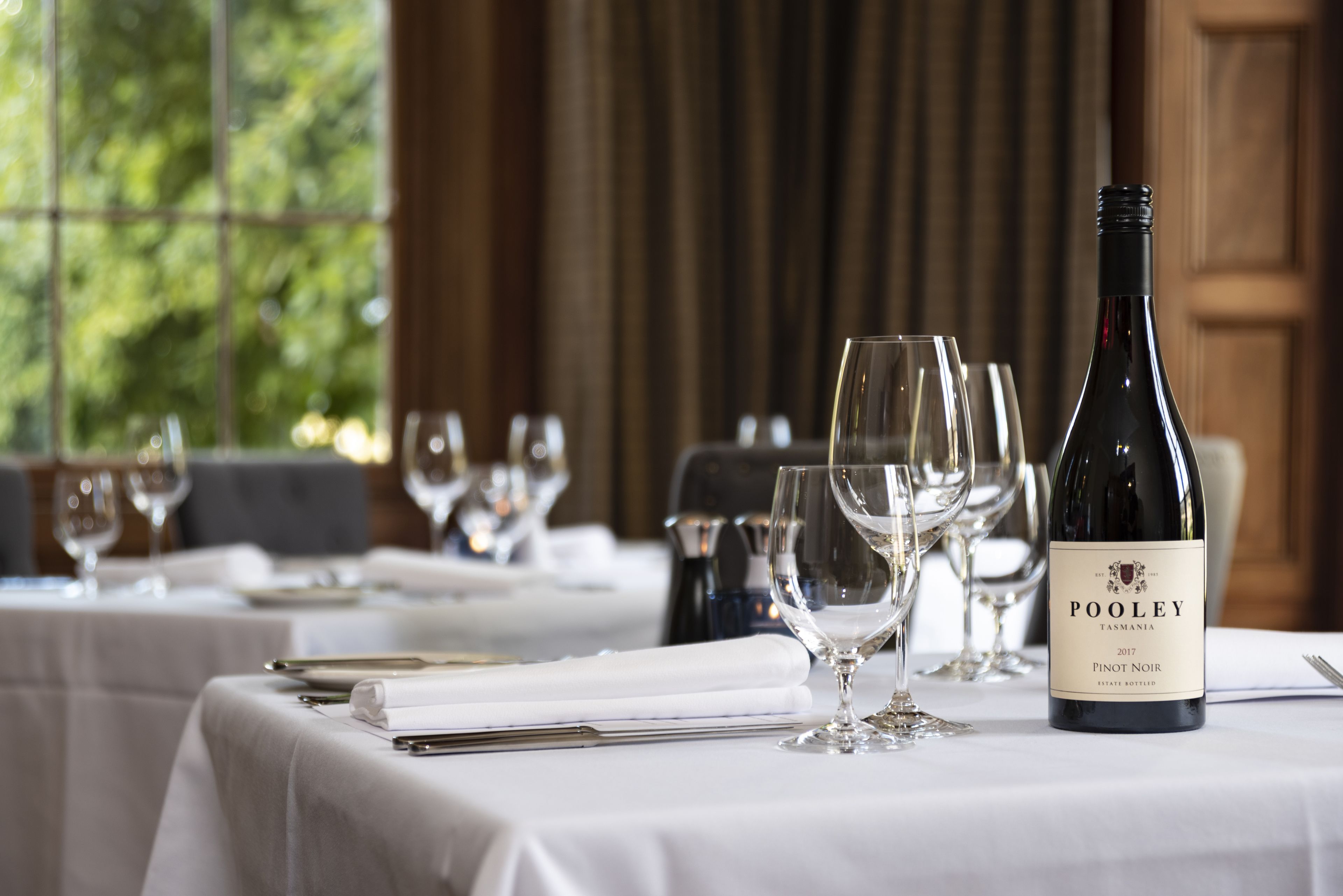 Une table à manger dressée avec des verres à vin et une bouteille de Pooley Pinot Noir.