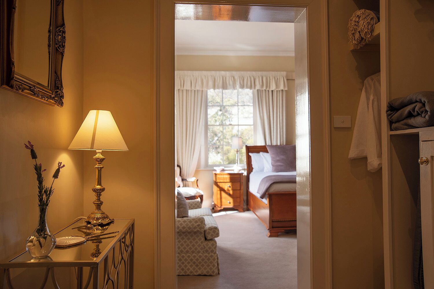 Une chambre d’hôtel avec un lit, une table de chevet avec une lampe, une chaise et une fenêtre avec des rideaux.