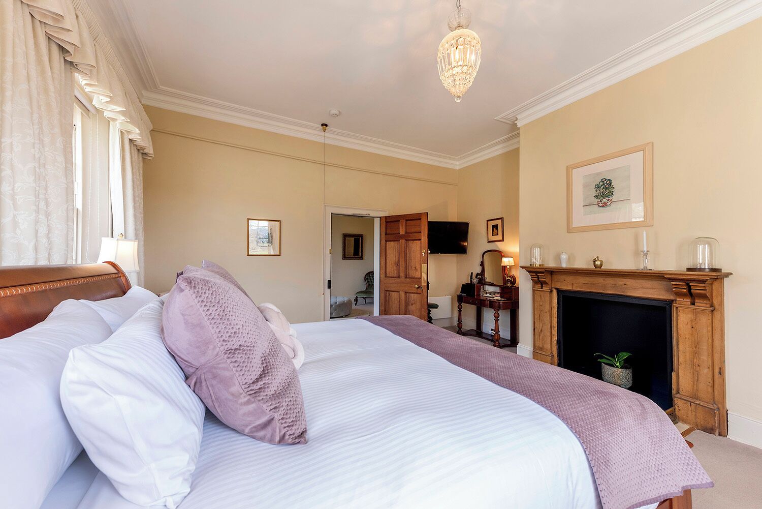 A hotel room with a large bed, a fireplace, a television, and a door leading to another room.