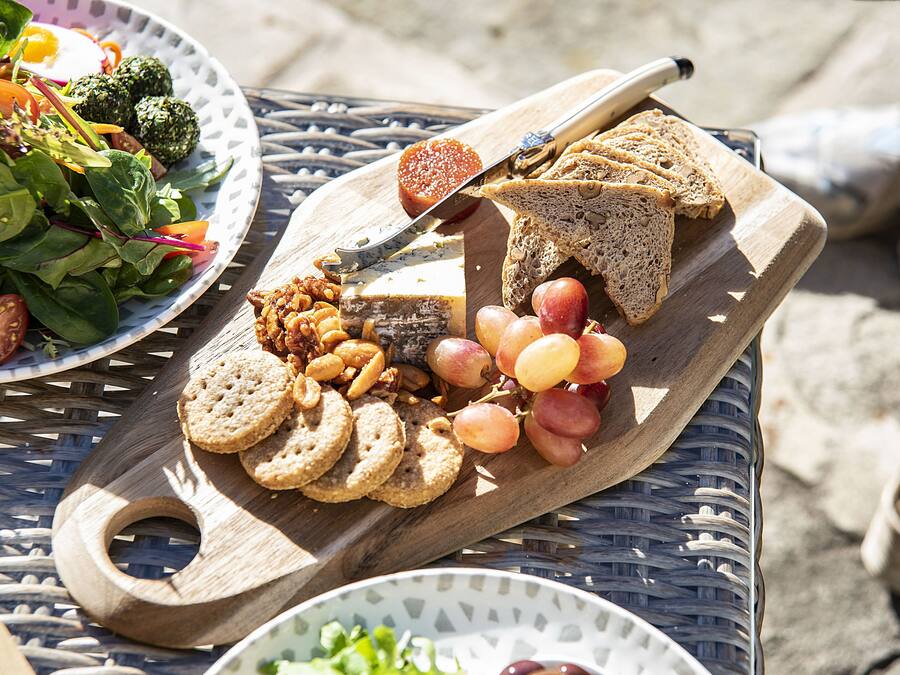 Ein Holzboden mit Brot, Trauben, Nüssen und Crackern auf einer Metalltischplatte.