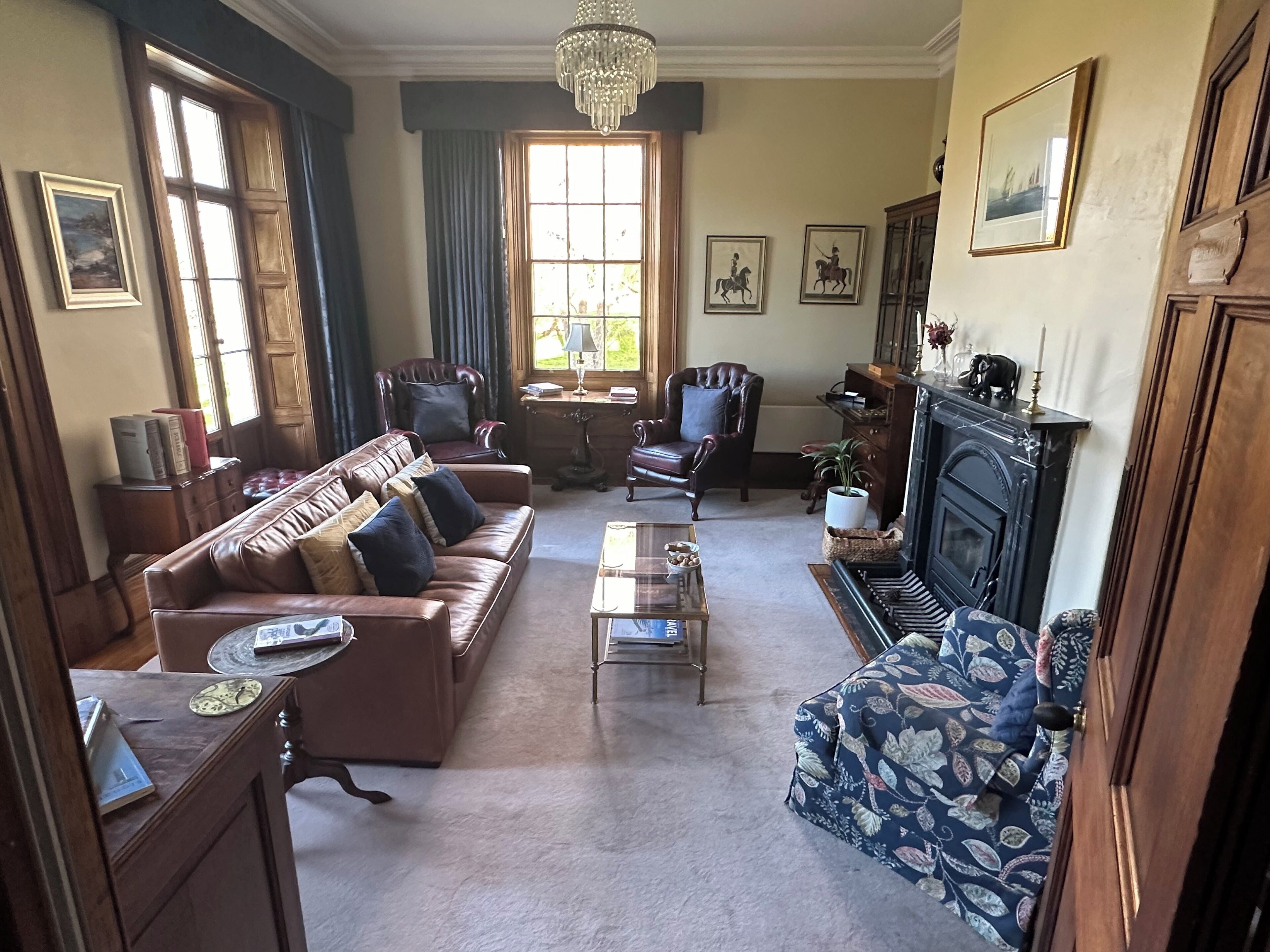 A traditional living room with a brown leather sofa, a patterned armchair, a piano, and a fireplace.