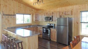 Una cocina con paredes de madera, una isla central con taburetes, electrodomésticos de acero inoxidable y un ventanal grande.