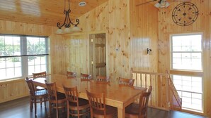 Un interior de madera con una mesa y sillas de comedor, un ventilador de techo y ventanas amplias.