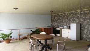 Una habitación con una mesa y sillas de madera, una planta en maceta, una kitchenette con refrigerador, microondas y armarios.