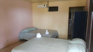 Una habitación con dos camas, un equipo de aire acondicionado pequeño y una puerta.