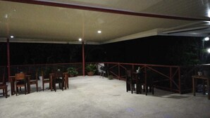 Un espacio de patio al aire libre con sillas y mesas de madera, rodeado por una barandilla roja.