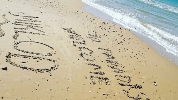A sandy beach with footprints and the word "WELCOME" written in the sand.