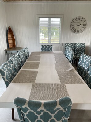 A dining area with a long table, patterned cushions, and a wall clock.