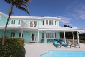 A two-story house with a pool, a covered patio with lounge chairs, and a small balcony.