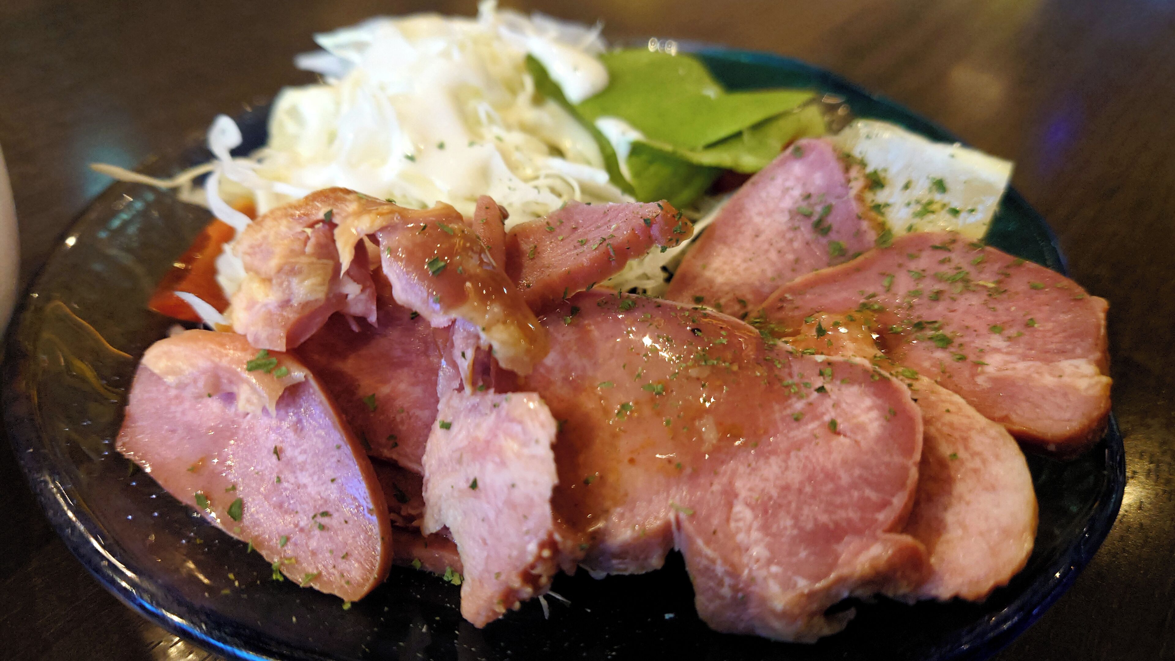 A plate of sliced ham garnished with herbs, accompanied by shredded vegetables and leafy greens.