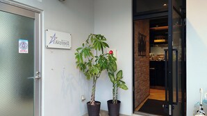 Een moderne entree met een glazen deur, een bord en twee planten in potten.