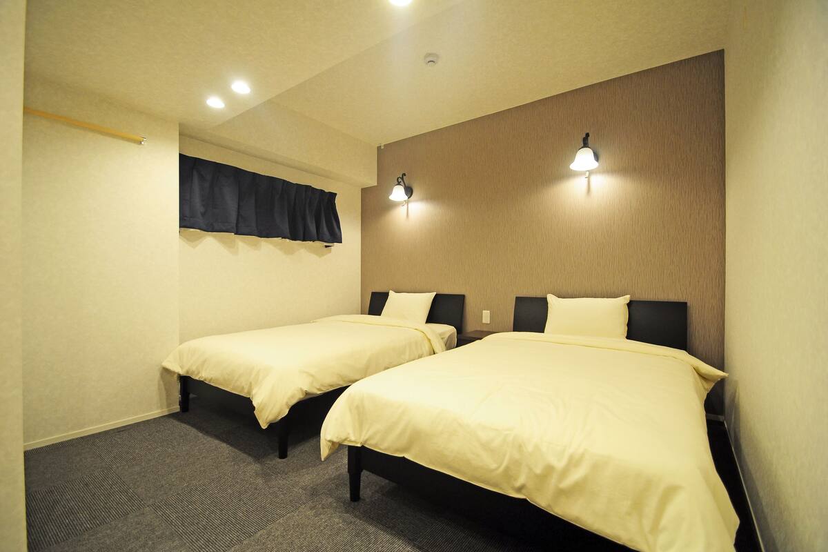 Une chambre d’hôtel avec deux lits simples, une fenêtre avec des rideaux occultants et deux lampes fixées au mur.