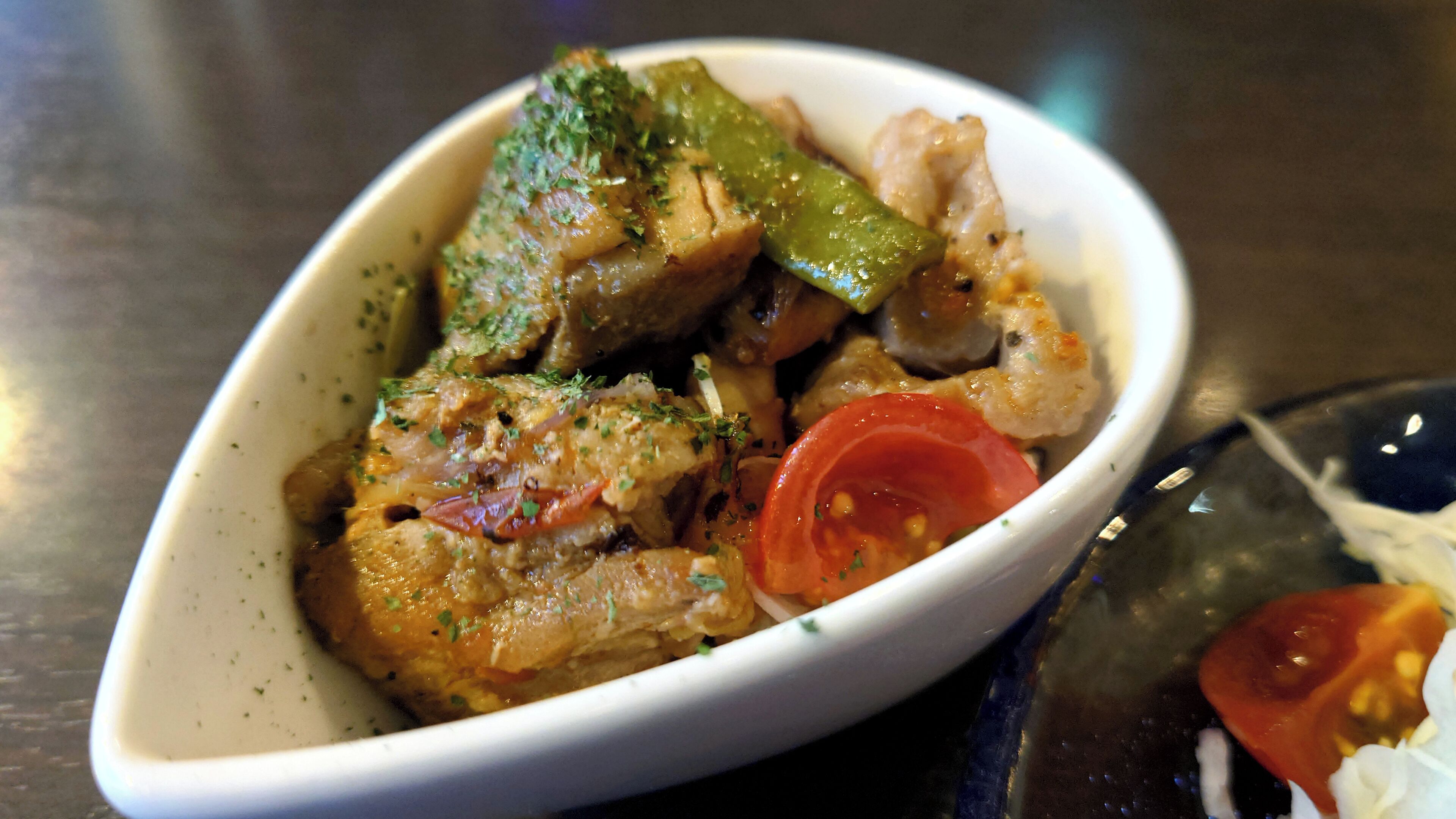 Un plato ovalado blanco con comida que incluye carne, verduras verdes y tomates.