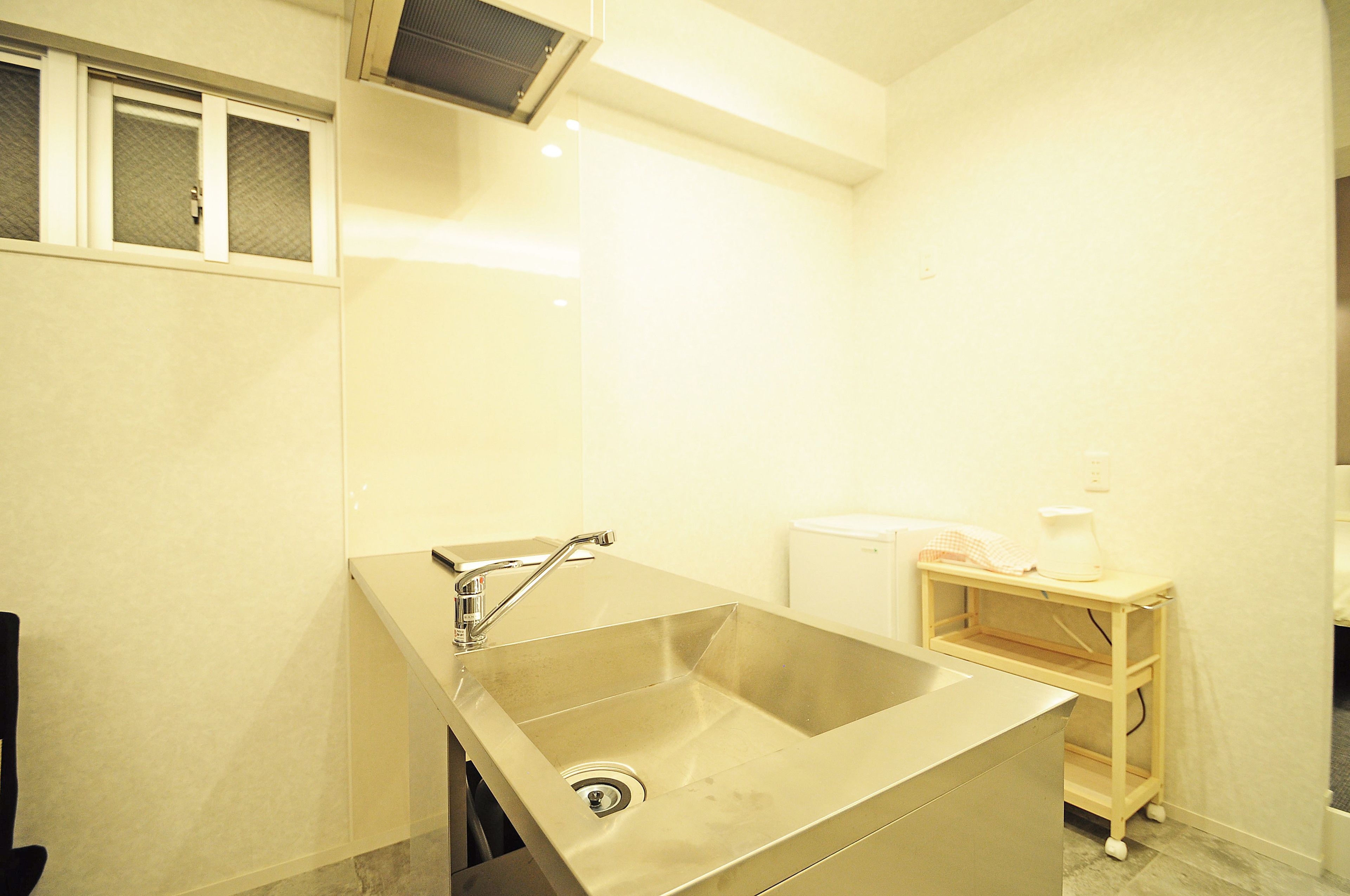 A small, modern bathroom with a stainless steel sink, a toilet, and a small shelf with a towel and a bottle.