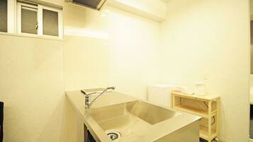A small, modern bathroom with a stainless steel sink, a toilet, and a small shelf with a towel and a bottle.