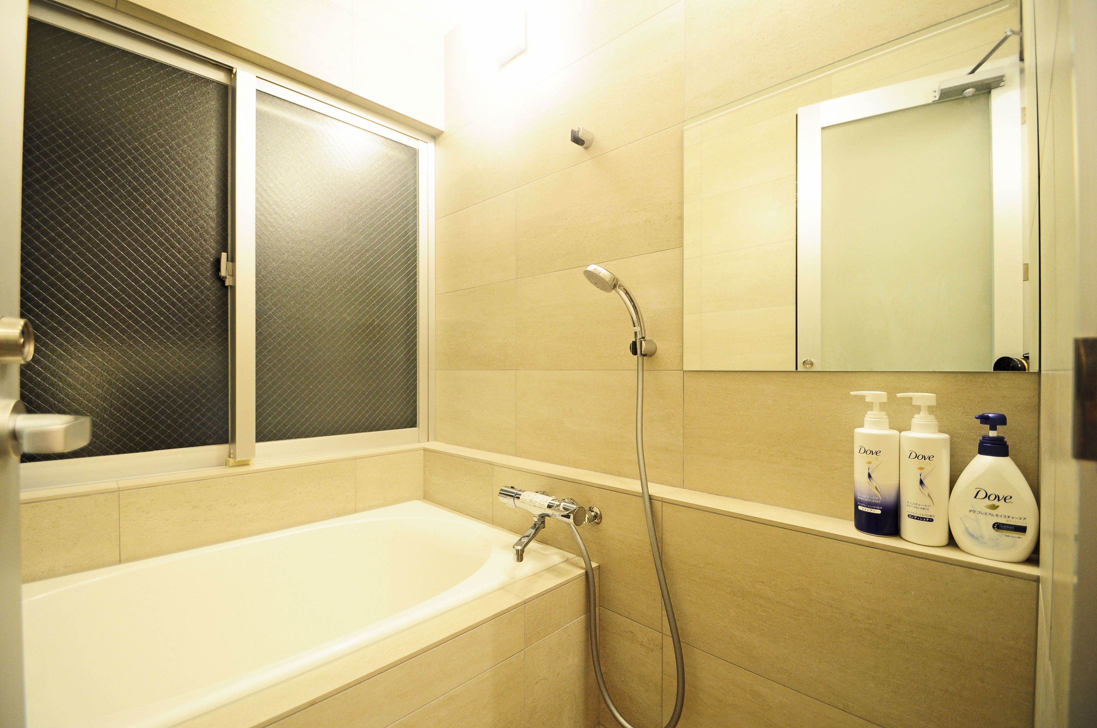 A bathroom with a bathtub, a shower, and a mirror. There are three Dove shampoo bottles on the wall.