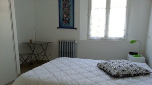 Et soveværelse med seng, radiator, vindue, bord og stol.